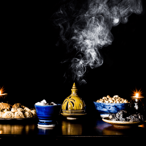 Traditional incense burner with rising smoke, surrounded by dates, nuts, and sweets.