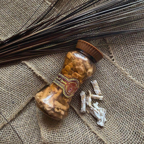 A glass jar of premium oudh wood chips on burlap fabric with aromatic incense sticks.
